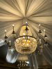 LARGE CRYSTAL CHANDELIER WITH STRANDS AND DROPLETS HANGING FROM EACH ARM. THE METAL FRAME IS GOLD-TONE