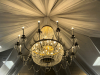 LARGE CRYSTAL CHANDELIER WITH STRANDS AND DROPLETS HANGING FROM EACH ARM. THE METAL FRAME IS GOLD-TONE