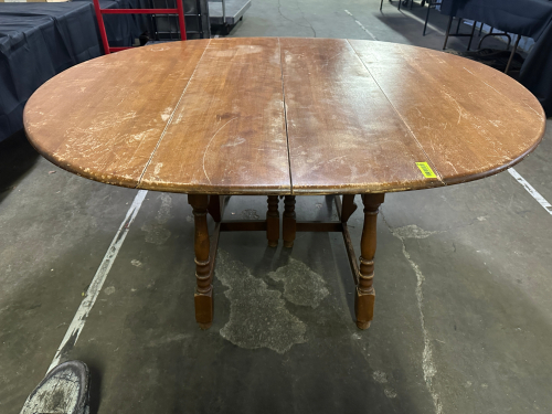 VINTAGE WOOD DROP-LEAF DINING TABLE WITH OVAL TOP AND TURNED LEGS. FEATURES FOLD-DOWN LEAVES FOR SPACE-SAVING USE. SOLID WOOD CONSTRUCTION. SHOWS NOTICEABLE SURFACE WEAR, SCRATCHES, AND FINISH LOSS CONSISTENT WITH AGE