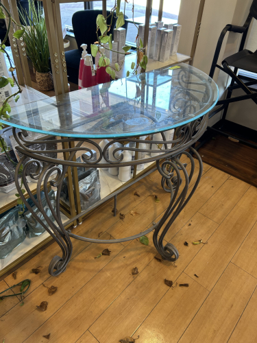 DECORATIVE METAL CONSOLE TABLE WITH OVAL GLASS TOP. FEATURES SCROLLWORK BASE AND CURVED LEGS.