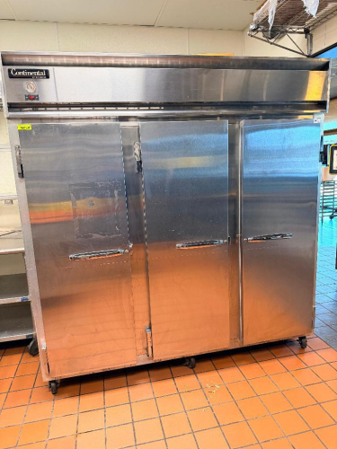 CONTINENTAL THREE DOOR REACH-IN REFRIGERATOR WITH TOP-MOUNT COMPRESSOR HOUSING. UNIT FEATURES THREE SOLID SWING DOORS, MULTIPLE INTERIOR WIRE SHELVES, AND CASTERS