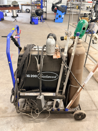 EASTWOOD TIG WELDER PACKAGE MOUNTED ON MOBILE CART WITH GAS CYLINDER, REGULATOR, TORCH, AND LEADS. CONTROL PANEL FEATURES ADJUSTABLE SETTINGS FOR POWER, CLEARANCE EFFECT, PRE FLOW, AND POST FLOW WITH AC/DC SELECTION.