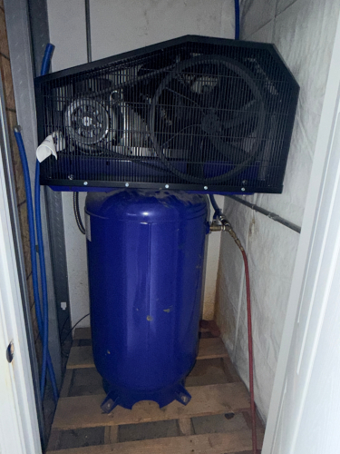 VERTICAL AIR COMPRESSOR WITH BELT-DRIVEN MOTOR, PROTECTIVE FAN SHROUD, AND MOUNTED TANK. UNIT INCLUDES HOSES, FITTINGS, AND MANUAL AS SHOWN. COMPRESSOR ASSEMBLY MOUNTED ON STORAGE SKID.