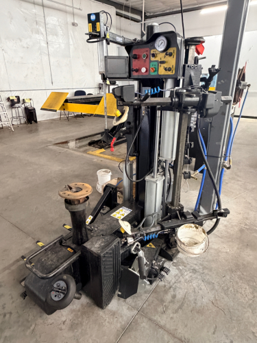 HEAVY DUTY TIRE CHANGER MACHINE WITH INTEGRATED BEAD BREAKER, SWING ARM ASSEMBLY, AND CONTROL PANEL WITH PRESSURE GAUGE. WITH ATTACHED ACCESSORIES AND AIR LINES PRESENT. INDUSTRIAL GRADE CONSTRUCTION WITH ELECTRO-PNEUMATIC OPERATION.