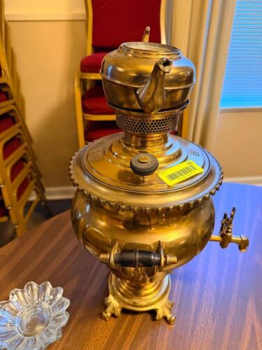 ANTIQUE BRASS SAMOVAR WITH INTEGRATED TEAPOT, FEATURING A POLISHED METAL BODY, SIDE HANDLES WITH INSULATED GRIPS, FRONT SPIGOT, AND VENTED HEATING CHAMBER WITH DECORATIVE BASE AND FEET