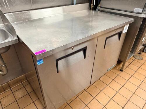 TRUE STAINLESS STEEL WORKTOP REFRIGERATOR WITH BACKSPLASH AND DOUBLE DOOR STORAGE COMPARTMENT. UNIT FEATURES SOLID DOORS WITH INTERNAL SHELVING AND REAR MOUNTED REFRIGERATION SYSTEM.