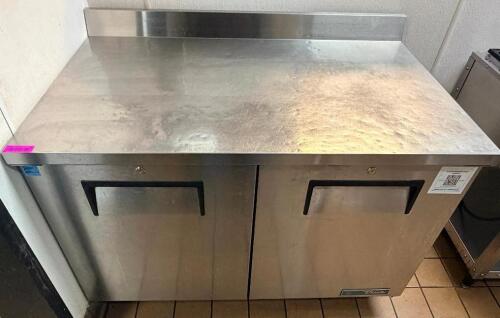 TRUE STAINLESS STEEL WORKTOP REFRIGERATOR WITH BACKSPLASH AND DOUBLE DOOR STORAGE COMPARTMENT. UNIT FEATURES SOLID DOORS WITH INTERNAL SHELVING AND REAR MOUNTED REFRIGERATION SYSTEM.