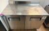 TRUE STAINLESS STEEL WORKTOP REFRIGERATOR WITH BACKSPLASH AND DOUBLE DOOR STORAGE COMPARTMENT. UNIT FEATURES SOLID DOORS WITH INTERNAL SHELVING AND REAR MOUNTED REFRIGERATION SYSTEM.