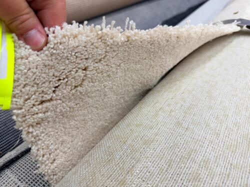 ROLL OF CARPETING IN LIGHT CREAM COLOR WITH SOFT TEXTURED SURFACE, PARTIAL ROLL WITH FRAYED EDGES AND EXPOSED BACKING