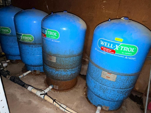 AMTROL FOUR PRESSURE TANKS, SHOWING SURFACE RUST AND WEAR, CONNECTED WITH PVC PIPING