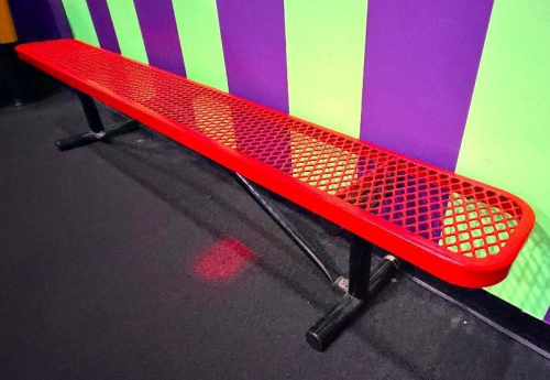 8 FT RED POWDER-COATED EXPANDED METAL BENCH WITH TUBULAR STEEL FRAME AND FLOOR-MOUNT STYLE SUPPORT LEGS.