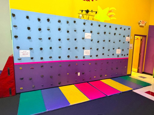 INDOOR CHILDREN&rsquo;S BOULDERING / CLIMBING WALL WITH PADDED FLOOR MATS, MOLDED HANDHOLDS, AND SAFETY MARKINGS. WALL FEATURES MULTIPLE ROUTE CONFIGURATIONS FOR RECREATIONAL PLAY.