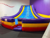 COMMERCIAL INFLATABLE SLIPPERY SLOPE SLIDE WITH PADDED ENTRY, HIGH SIDEWALLS, AND ENCLOSED LANDING AREA. UNIT FEATURES MULTI-COLOR VINYL CONSTRUCTION WITH TOP SAFETY NETTING.