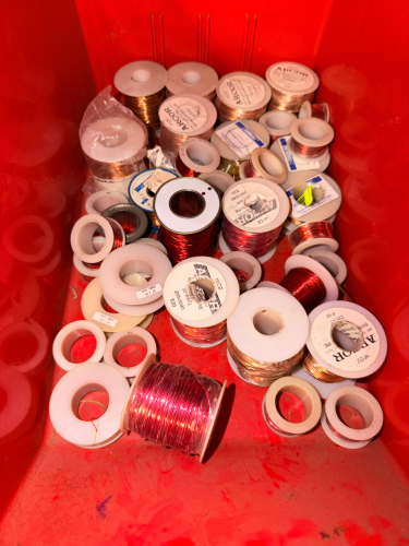 RED PLASTIC TOTE AND CONTENTS - LOT OF ASSORTED MAGNET WIRE SPOOLS INCLUDING COPPER AND COLORED ENAMELED WIRE. MIXED LOT CONTAINING PARTIAL AND NEAR-FULL SPOOLS OF VARIOUS GAUGES AND LENGTHS
