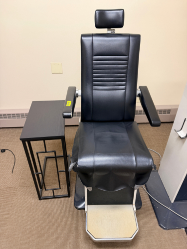 BURTON OPHTHALMIC EXAM CHAIR WITH PADDED VINYL UPHOLSTERY, ADJUSTABLE HEADREST, PADDED ARMRESTS, AND INTEGRATED FOOT PLATFORM. MANUAL RECLINING AND HEIGHT ADJUSTMENT FEATURES WITH METAL BASE CONSTRUCTION.