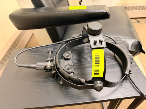 HEINE OMEGA 150 BINOCULAR INDIRECT OPHTHALMOSCOPE HEADSET WITH ADJUSTABLE HEADBAND, OPTICAL VIEWING SYSTEM, AND INTEGRATED POWER CABLE. INCLUDES PADDED SUPPORT FRAME AND CONTROL ADJUSTMENTS.