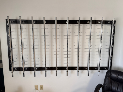 (2) WALL-MOUNTED EYEGLASS DISPLAY RACK WITH TEN ROTATING CHROME DISPLAY PANELS AND DARK WOOD BACKING.