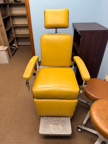 BELMONT VINTAGE MEDICAL / OPHTHALMIC EXAMINATION CHAIR WITH ADJUSTABLE HEADREST AND HYDRAULIC PEDESTAL BASE. UPHOLSTERED IN MUSTARD YELLOW VINYL WITH CHROME METAL FRAME AND FOOTREST.