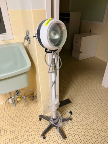 VINTAGE MEDICAL EXAMINATION LIGHT ON ROLLING STAND WITH ADJUSTABLE HEAD, CONTROL SWITCH, AND POWER CORD.