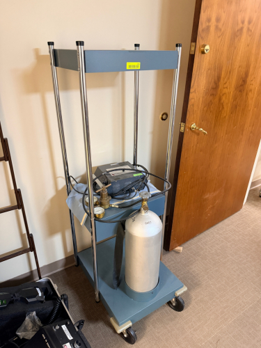 MEDICAL GAS CYLINDER CART WITH REGULATOR ASSEMBLY, PRESSURE GAUGES, CONTROL VALVES, AND MOBILE STORAGE FRAME.