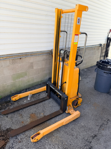 ULINE ELECTRIC STRADDLE STACKER WITH POWER LIFT AND POWER DRIVE FUNCTIONS. WALK-BEHIND DESIGN WITH STRADDLE LEGS, FORKS, BATTERY COMPARTMENT, SAFETY GUARDING, AND OPERATOR CONTROLS.