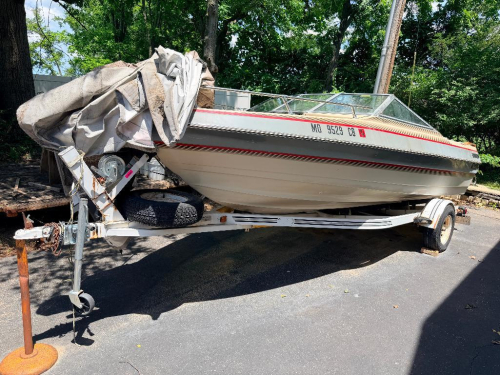 BARETTA BOWRIDER BOAT WITH WALK-THROUGH WINDSHIELD, OPEN COCKPIT SEATING, SWIM PLATFORM, REAR BOARDING LADDER, AND SINGLE STERN DRIVE. INCLUDES MATCHING ROLCO SINGLE-AXLE TRAILER. BOAT SHOWS WEATHERING, DUST ACCUMULATION, AGING INTERIOR UPHOLSTERY, AND SU