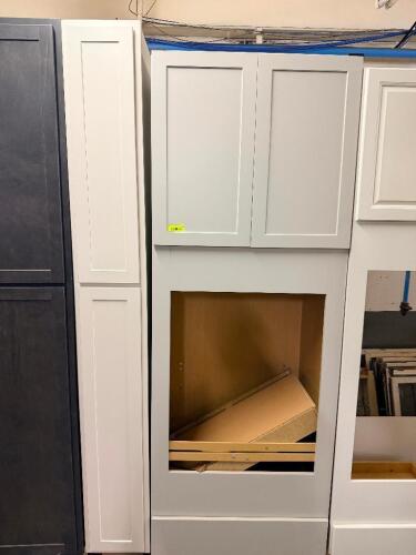 WHITE SHAKER-STYLE OVEN CABINET ASSEMBLY WITH OVERHEAD DOUBLE-DOOR STORAGE CABINET AND MATCHING FULL-HEIGHT FILLER PANEL. FEATURES A LARGE CENTER OPENING DESIGNED TO ACCEPT A BUILT-IN OVEN UNIT AND A PAINTED WHITE FINISH.