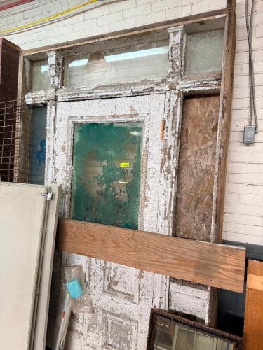 ANTIQUE WOOD ENTRY DOOR ASSEMBLY WITH TRANSOM WINDOW, SIDE LITES, AND ORIGINAL WOOD FRAME. ASSEMBLY FEATURES DECORATIVE WOOD MOLDING, MULTIPLE GLASS PANELS, AND ORIGINAL PAINT WITH EXTENSIVE AGE-RELATED WEAR.