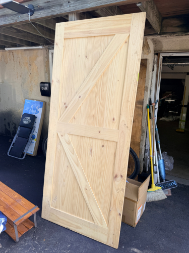 WOOD SLIDING BARN DOOR CONSTRUCTED OF NATURAL WOOD WITH VERTICAL PLANK DESIGN AND DIAGONAL CROSS BRACING. UNFINISHED.