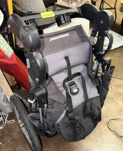EXPEDITION SINGLE CHILD JOGGING STROLLER WITH THREE-WHEEL DESIGN, PADDED SEAT, SAFETY HARNESS, STORAGE BASKET, CUP HOLDERS, AND CANOPY FRAME.