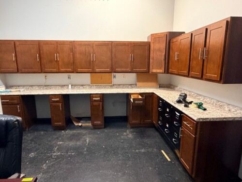 MATCHING WOODGRAIN OFFICE CABINET SET INCLUDING MULTIPLE WALL CABINETS, BASE CABINETS, LATERAL FILE DRAWERS, LAMINATE COUNTERTOPS WITH BACKSPLASH, AND METAL CABINET HARDWARE.