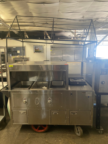 STAINLESS STEEL MOBILE CONCESSION FOOD CART WITH ENCLOSED STORAGE, OVERHEAD DISPLAY FRAME, SERVING SHELF, THREE PAN WELLS, DOUBLE BASIN HAND SINK, LOCKING CASH DRAWER, AND ROLLING CASTERS. UNIT FEATURES A STAINLESS STEEL CONSTRUCTION WITH VINYL SKIRTING