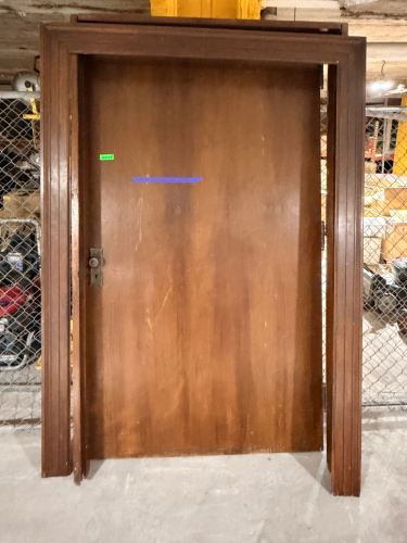 VINTAGE SOLID WOOD DOOR WITH MATCHING WOOD FRAME, RAISED TRIM DETAIL, DARK BROWN FINISH, AND PERIOD-STYLE METAL HARDWARE. DOOR FEATURES A ROUND METAL KNOB, RECTANGULAR BACKPLATE, KEYHOLE, AND MORTISE-STYLE LOCK HARDWARE.