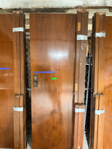VINTAGE SOLID WOOD DOOR WITH DARK BROWN FINISH, CONTRASTING DECORATIVE INLAY, MATCHING WOOD TRIM COMPONENTS, AND PERIOD-STYLE METAL HARDWARE. DOOR FEATURES A RECTANGULAR RECESSED DECORATIVE BORDER, ROUND METAL KNOB, RECTANGULAR BACKPLATE, KEYHOLE, AND MOR
