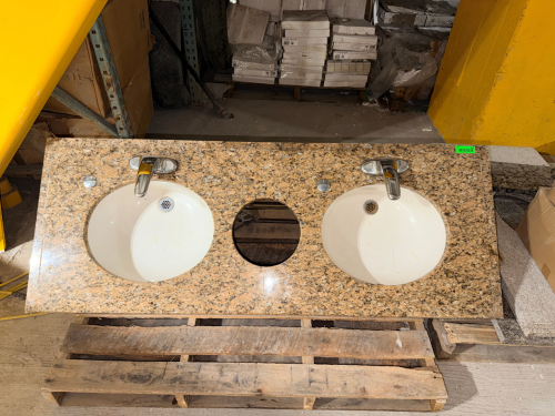 POLISHED GRANITE DOUBLE-SINK VANITY COUNTERTOP WITH GOLD, TAN, BLACK, GRAY, AND CREAM NATURAL STONE PATTERN. INCLUDES TWO WHITE ROUND UNDERMOUNT SINK BASINS, TWO CHROME SINGLE-HANDLE FAUCETS, DRAIN FITTINGS, AND A LARGE CENTER ACCESS OPENING. COUNTERTOP H