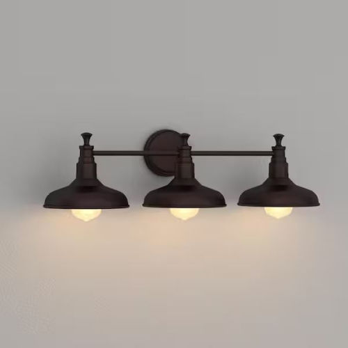 DESIGN HOUSE KIMBALL COLLECTION THREE-LIGHT VANITY LIGHT WITH GALVANIZED FINISH, THREE METAL SHADES, HORIZONTAL SUPPORT BAR, AND ROUND WALL-MOUNT BACKPLATE.