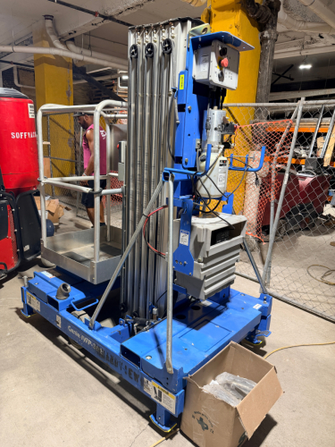 GENIE VERTICAL PERSONNEL LIFT WITH TELESCOPING ALUMINUM MAST, ALUMINUM WORK PLATFORM WITH GUARDRAILS, PLATFORM CONTROLS, GROUND CONTROLS, EMERGENCY STOP, OUTRIGGERS, HYDRAULIC LIFT SYSTEM, BATTERY CHARGER, AND MANUAL-ROLLING BASE.