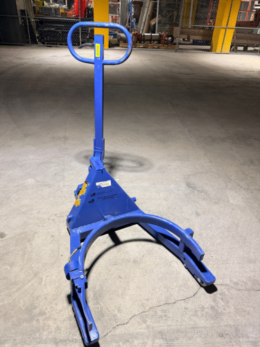 HYDRAULIC DRUM TRANSPORTER WITH MANUAL PUMP HANDLE, CURVED DRUM SUPPORT FRAME, HYDRAULIC GRIPPING ARMS, FLOOR-LEVEL PICKUP DESIGN, STEERABLE REAR WHEELS, AND FRONT LOAD ROLLERS.