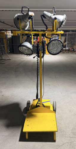 GRAINGER PORTABLE FOUR-HEAD INDUSTRIAL WORK LIGHT / FLOODLIGHT TOWER WITH FOUR ADJUSTABLE METAL REFLECTOR LAMP HEADS, PROTECTIVE WIRE GUARDS, INDIVIDUAL HANDLES, COILED POWER CORDS, WHEELED STEEL BASE, VERTICAL SUPPORT MAST, AND LOWER EQUIPMENT PLATFORM.