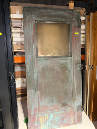 VINTAGE HEAVY-DUTY METAL DOOR WITH LARGE UPPER VISION PANEL, RAISED PANEL DETAILING, AND HEAVY HINGE HARDWARE. DOOR HAS AN AGED VERDIGRIS/PATINA FINISH WITH EXTENSIVE SURFACE WEAR, DISCOLORATION, SCRATCHES, AND RESIDUE.