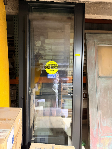 FULL-GLASS ALUMINUM AUTOMATIC COMMERCIAL DOOR ASSEMBLY WITH BLACK FINISH, LARGE TEMPERED GLASS PANEL, CONTINUOUS HINGE, AND ASSOCIATED AUTOMATIC DOOR HARDWARE