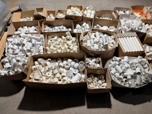 LARGE ASSORTED LOT OF PVC AND PLASTIC PIPE FITTINGS INCLUDING COUPLINGS, ELBOWS, TEES, REDUCERS, ADAPTERS, CAPS, BUSHINGS, AND OTHER MISCELLANEOUS FITTINGS IN VARIOUS SIZES. LOT CONSISTS PRIMARILY OF WHITE PVC FITTINGS WITH ADDITIONAL CREAM, GRAY, AND ORA