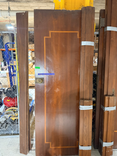 VINTAGE SOLID WOOD DOOR WITH DARK BROWN FINISH, CONTRASTING DECORATIVE INLAY, MATCHING WOOD TRIM COMPONENTS, AND PERIOD-STYLE METAL HARDWARE. DOOR FEATURES A RECTANGULAR RECESSED DECORATIVE BORDER, ROUND METAL KNOB, RECTANGULAR BACKPLATE, KEYHOLE, AND MOR