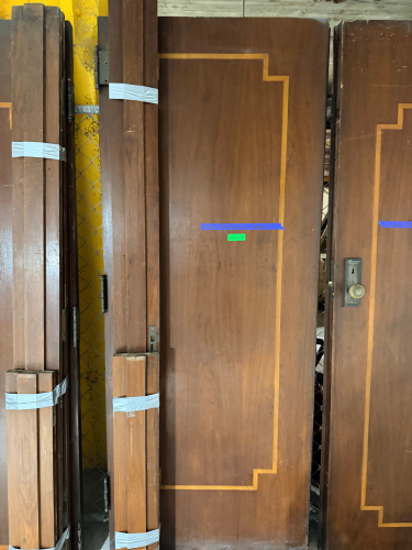 VINTAGE SOLID WOOD DOOR WITH DARK BROWN FINISH, CONTRASTING DECORATIVE INLAY, MATCHING WOOD TRIM COMPONENTS, AND PERIOD-STYLE METAL HARDWARE. DOOR FEATURES A RECTANGULAR RECESSED DECORATIVE BORDER, ROUND METAL KNOB, RECTANGULAR BACKPLATE, KEYHOLE, AND MOR