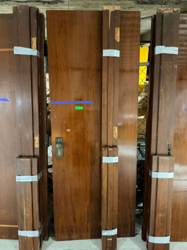 VINTAGE SOLID WOOD DOOR WITH DARK BROWN FINISH, CONTRASTING DECORATIVE INLAY, MATCHING WOOD TRIM COMPONENTS, AND PERIOD-STYLE METAL HARDWARE. DOOR FEATURES A RECTANGULAR RECESSED DECORATIVE BORDER, ROUND METAL KNOB, RECTANGULAR BACKPLATE, KEYHOLE, AND MOR