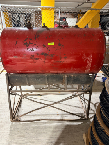 RED HORIZONTAL STEEL FUEL OIL STORAGE TANK WITH MULTIPLE TOP-MOUNTED FITTINGS, LOWER VALVE AND HOSE ASSEMBLY, STEEL SUPPORT FRAME, AND INTEGRATED CONTAINMENT PAN