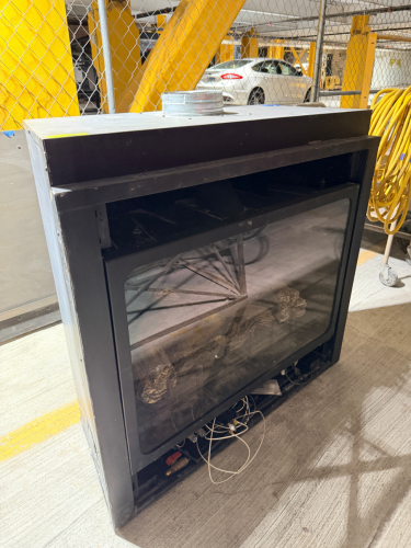 BUILT-IN GAS FIREPLACE INSERT WITH BLACK METAL ENCLOSURE, LARGE GLASS FRONT, CERAMIC LOG SET, INTERNAL BURNER ASSEMBLY, AND TOP VENT CONNECTION.