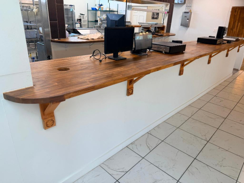 20' CUSTOM SOLID WOOD BUTCHER BLOCK COUNTERTOP SYSTEM WITH MULTIPLE CONNECTED SECTIONS, ROUNDED END SECTIONS, AND WALL-MOUNTED WOOD SUPPORT BRACKETS. COUNTERTOP FEATURES LAMINATED SOLID WOOD CONSTRUCTION WITH STAINED AND SEALED FINISH. INCLUDES MATCHING D