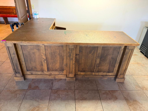 CUSTOM-BUILT L-SHAPED WOOD BAR WITH RAISED-PANEL CABINETRY, MULTIPLE STORAGE COMPARTMENTS, DRAWERS, AND TEXTURED COUNTERTOP WITH WOOD EDGE TRIM