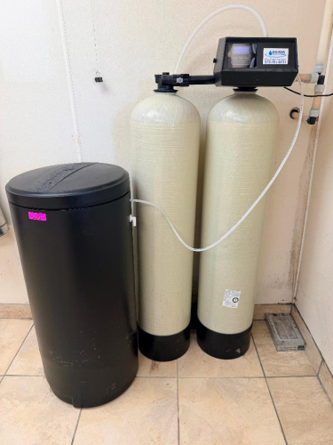 BAUMAN DUAL-TANK WATER SOFTENER SYSTEM WITH TWO FIBERGLASS MINERAL TANKS, SEPARATE BRINE TANK, AUTOMATIC DIGITAL CONTROL VALVE, INTERCONNECTING PLUMBING, AND BRINE LINE.